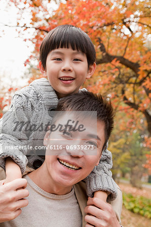 Little boy sitting on his fathers shoulders, walking through the park in autumn, Close up portrait