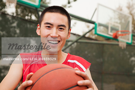 Young man sitting with a basketball on the basketball court, portrait