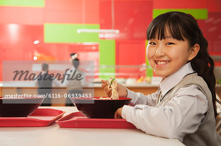 School girl eats noodles in school cafeteria