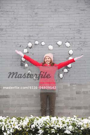 Young woman standing on wall with heart shaped snow balls
