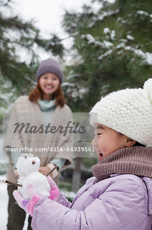 Girl Holding a snowman in a park with mother