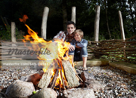 Father and son sitting by fire outdoors