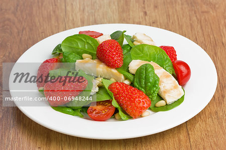 Spinach, grilled chicken, strawberry, cherry tomatoes and pine nuts salad on white plate