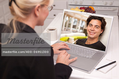 Happy Young Woman In Kitchen Using Laptop Online Dating Search with Portrait of Man On Screen.