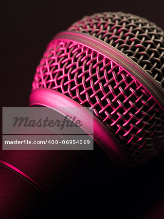 Macro photo of a vocal microphone lit with stage lights.