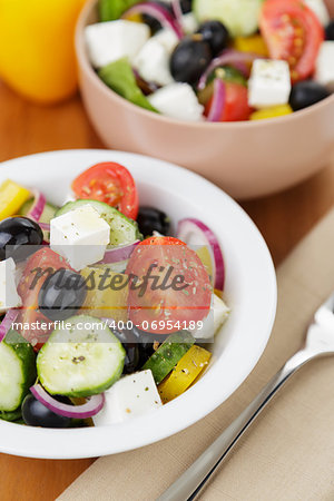 fresh greek salad in white bowl, on wood table