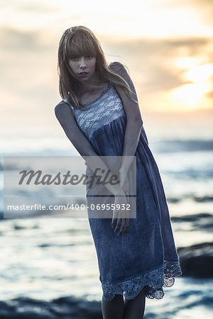 Beautiful young model standing on rocks by the sea on a glowing background