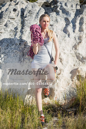 Blonde woman with climbing equipment leaning on rock