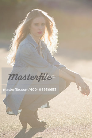 Blonde woman crouching down on a highway looking at camera
