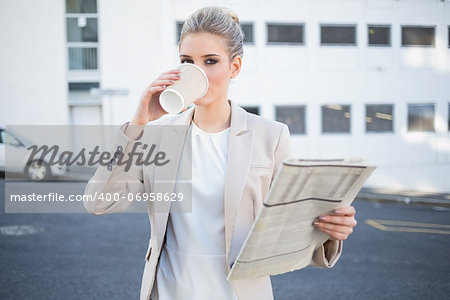 Serious stylish businesswoman drinking coffee outdoors on urban background