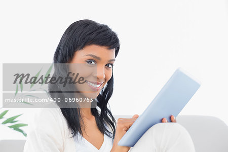 Pleased black haired woman in white clothes typing on a tablet pc in a living room
