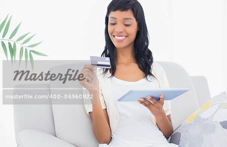 Delighted black haired woman buying online with her tablet pc in a living room