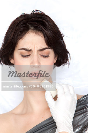 Woman wrapped in plastic with hand in latex glove applying make-up to her face with sponge, studio shot