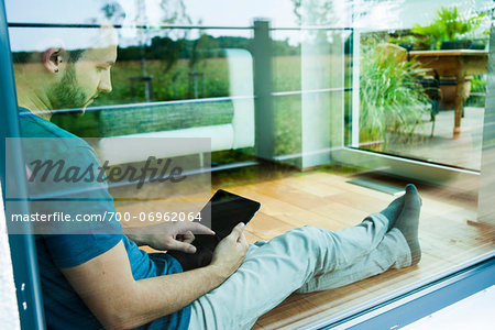 Young Man Sitting on Floor at Home using Tablet Computer, Mannheim, Baden-Wurttemberg, Germany