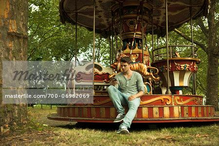 Young Man using Cell Phone while Sitting on Edge of Carousel, Mannheim, Baden-Wurttemberg, Germany