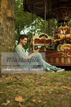 Young Man using Cell Phone while Sitting near Carousel, Mannheim, Baden-Wurttemberg, Germany