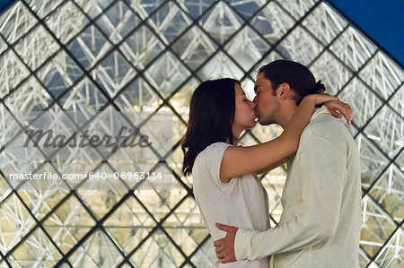 France, Paris, The Louvre, Couple kissing in front of glass pyramid