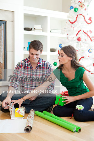 Young couple sitting on floor, wrapping Christmas presents