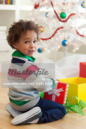 Young boy sitting under Christmas tree, opening Christmas presents