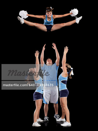 Studio shot of cheerleaders (16-17) assisting friend during jump