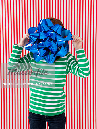 Studio shot of girl (4-5) holding large gift bow in front of face