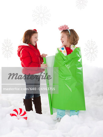 Studio shot of girl (4-5) wrapping friend (6-7) as Christmas gifts
