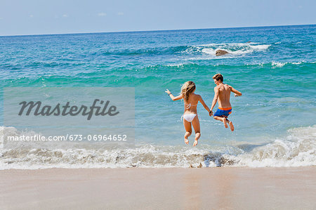 Young man and woman jumping in surf