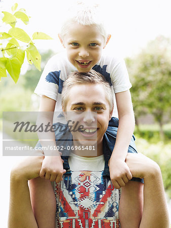Teenage boy carrying younger brother on shoulders