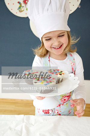 Little girl with chef's hat presenting muffins, Munich, Bavaria, Germany