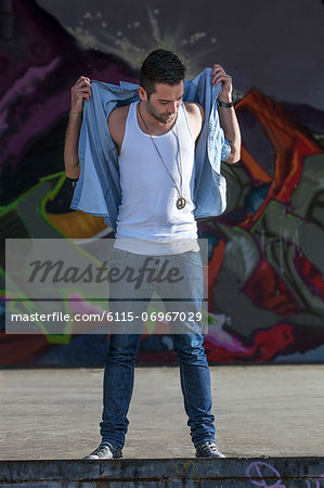 Young man standing in front of graffiti wall, Munich, Bavaria, Germany