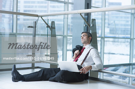 Businessman sitting on ground asleep with laptop