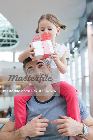 Young daughter sits on fathers shoulders and gives him a present Young daughter sits on fathers shoulders and gives him a present