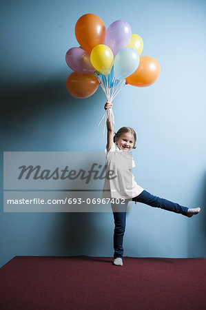 Young girl pretending to be lifted up by bunch of balloons