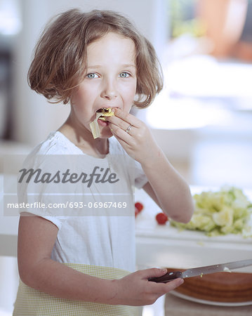 Young girl eating salad whilst holding knife in kitchen