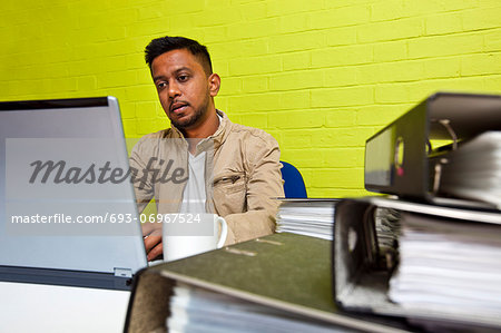 Young Indian man working at his computer surrounded by folders