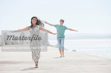 Happy young couple with arms outstretched on pier