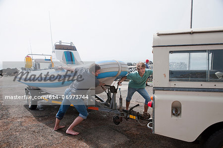 Two young men fixing dinghy trailer to vehicle