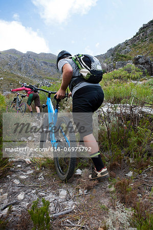 Young couple pushing mountain bikes up mountain path