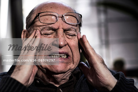 Senior man with eyes closed, wearing glasses, looking stressed