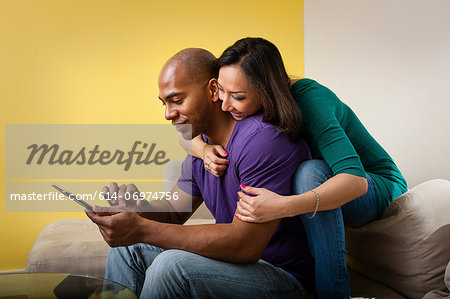 Mid adult couple sitting on sofa looking at digital tablet