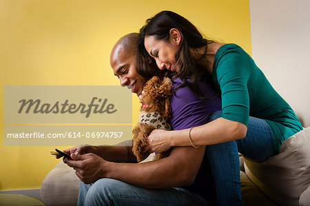 Mid adult couple sitting on sofa with dog and smartphone