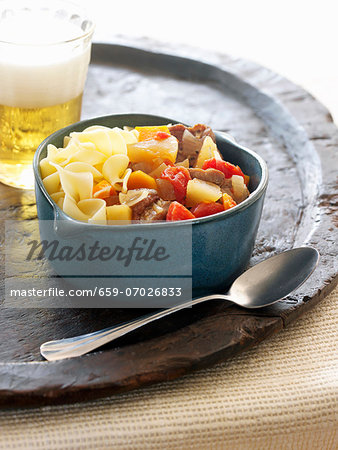 Noodles and Beef Goulash in a Bowl; Spoon and a Glass of Beer