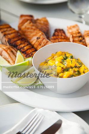 Grilled Salmon with Mango Salsa and Lime Wedges on a Platter on a Table Grilled Salmon with Mango Salsa and Lime Wedges on a Platter on a Table