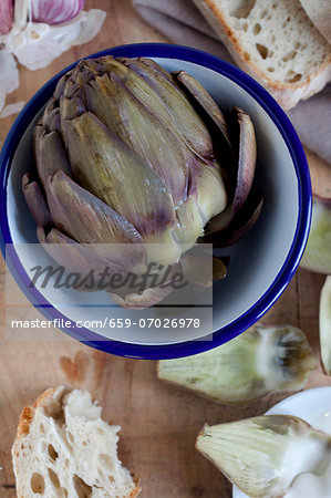 A cooked artichoke in a bowl with bread (view from above)