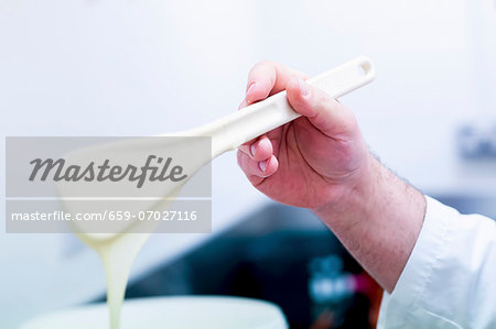 A hand holding a dough scraper covered in melted white chocolate