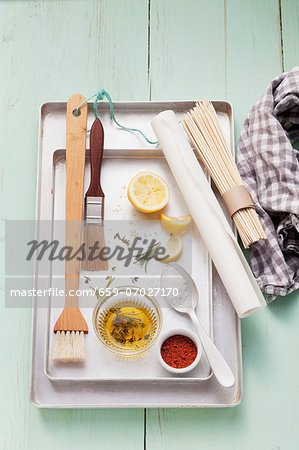 Assorted barbecue utensils, seasonings, lemons and olive oil on a grill pan