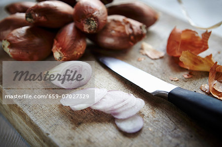 Whole and sliced shallots on a wooden board