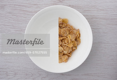 A halved portion of cornflakes in a white bowl (view from above)