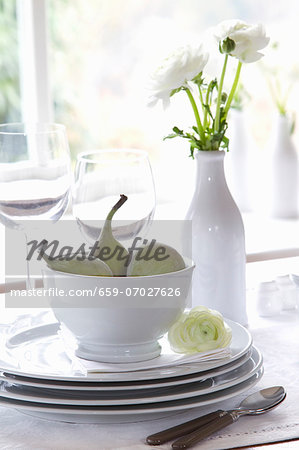 A stack of crockery with figs and a vase of white ranunculus flowers A stack of crockery with figs and a vase of white ranunculus flowers