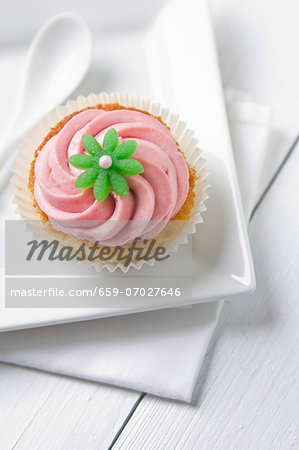 A cupcake topped with pink icing and a green flower